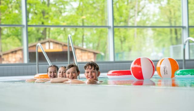 Vier lachende Kinder am Beckenrand vom Hallenbad
